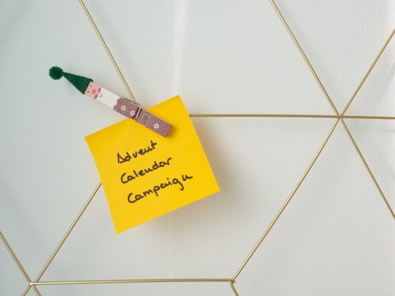 A yellow sticky note with "Advent Calendar Campaign" handwritten on it is pinned to a white and gold geometric board with a clip featuring a small Santa figure.